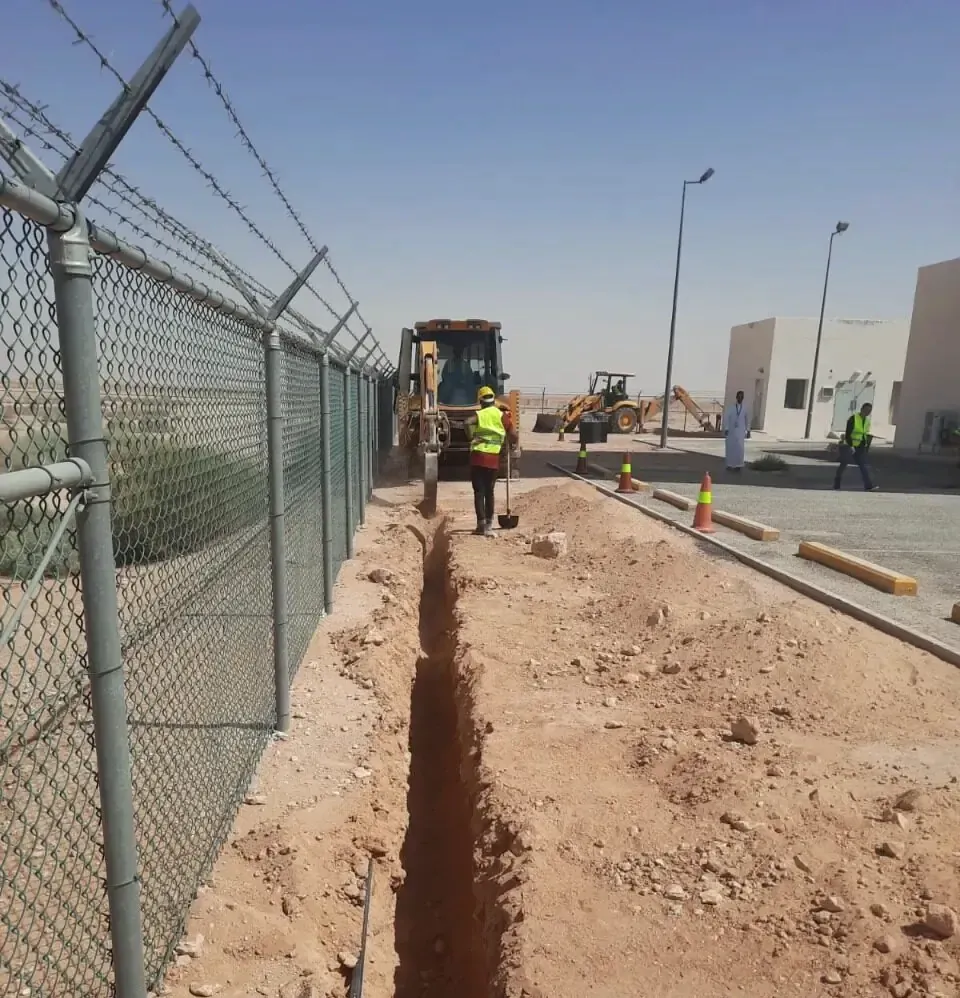 Cable trench excavated along a security fence with a backhoe working further along the line